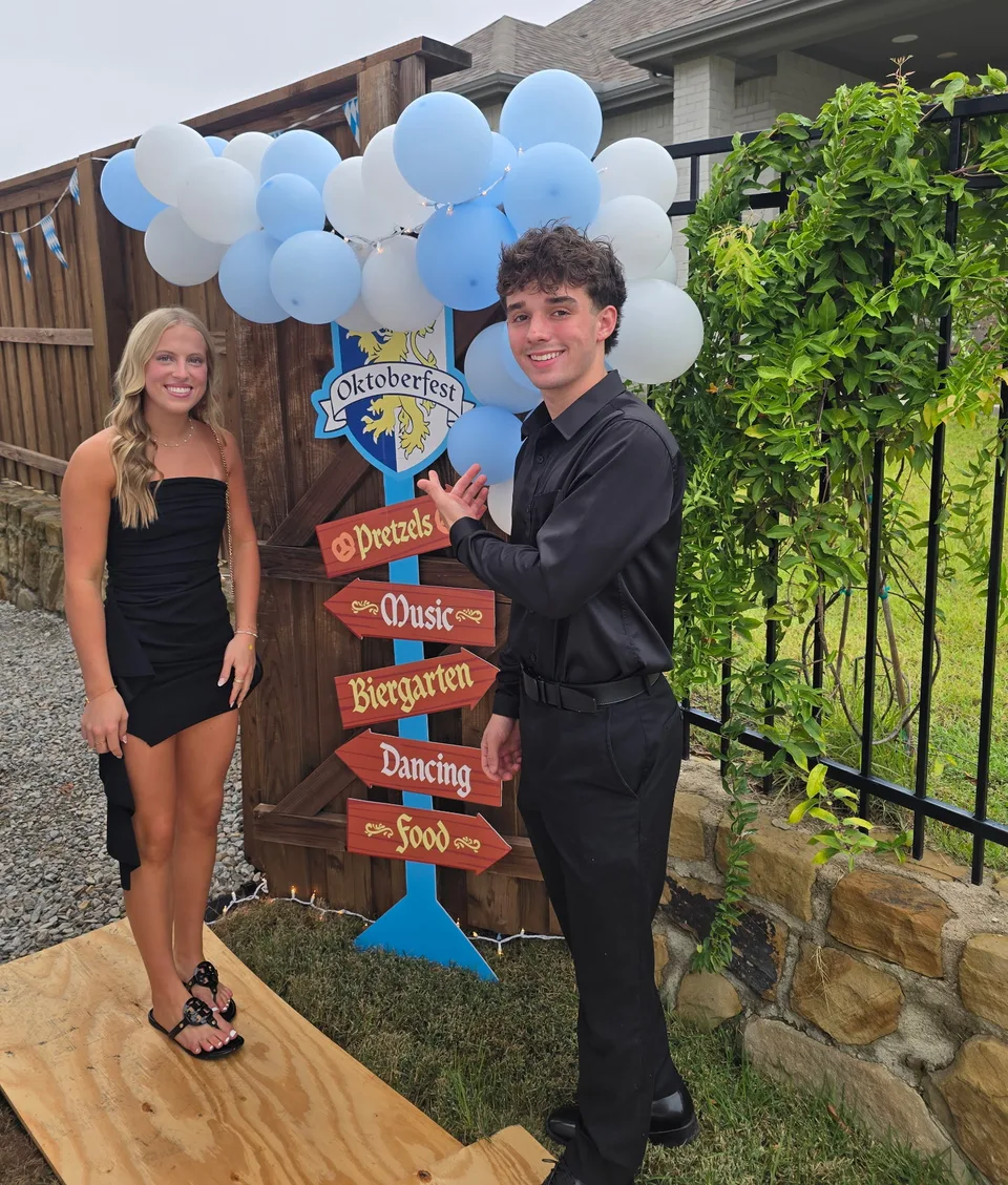 Sky and Makayla, dressed in black, at a Walsh Ranch backyard Oktoberfest party next to the party's welcome sign